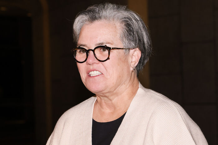 Rosie O&rsquo;Donnell wearing glasses and a beige sweater, speaking publicly about MAGA and Minnesota school shooter remark.