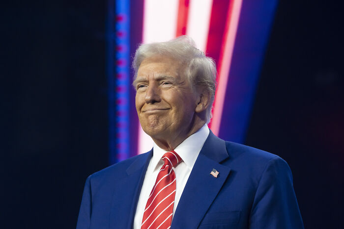 Former President Donald Trump in a blue suit and red striped tie at an event related to the presidential walk of fame.