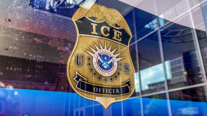 ICE officer badge displayed on a reflective glass window related to alleged detainment of autistic girl by ICE.