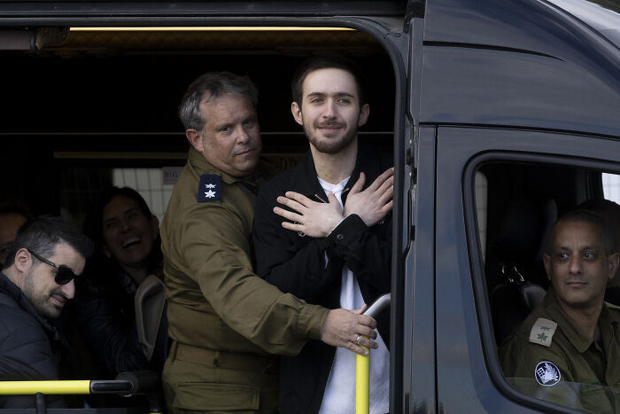 Man escorted by military personnel inside a vehicle, relating to controversy over free Palestine movement and hate groups.