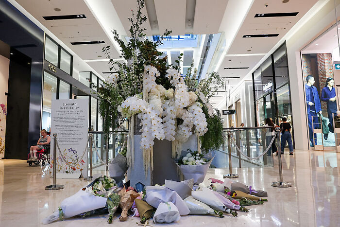 Floral memorial with white orchids and bouquets inside a shopping mall representing social media impact on Donald Trump.