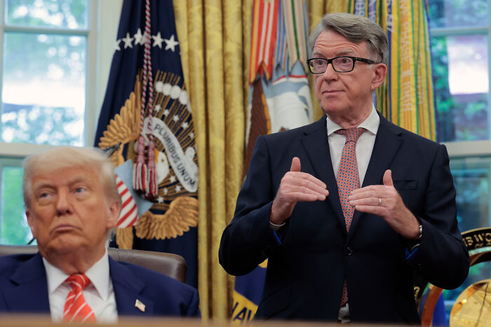 U.S. Ambassador speaking in the Oval Office with presidential flags and former President Trump seated nearby