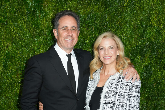 Jerry Seinfeld and wife Jessica at an event, with greenery background, relating to Free Palestine movement controversy.