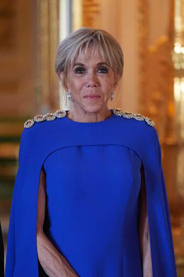 French First Lady wearing blue dress indoors, involved in legal dispute requiring scientific proof of womanhood.