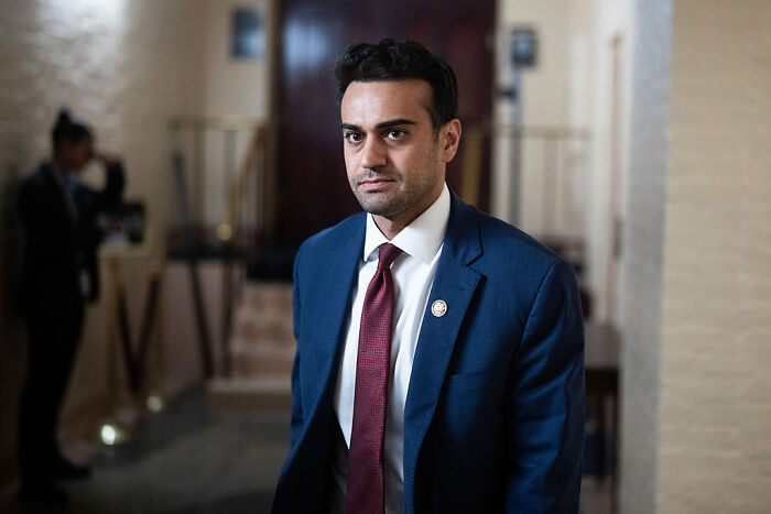Man in a blue suit and red tie indoors, symbolizing discussion about Charlie Kirk appearing on U.S. currency under GOP proposal