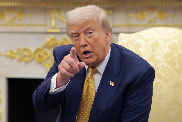 Donald Trump in a suit, pointing forward while discussing steep new tariffs on pharmaceutical imports and trucks.