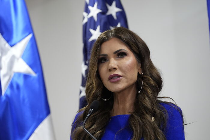 Woman speaking at a podium with U.S. and Texas flags in the background about multiple injuries and fatalities in Texas shooting.