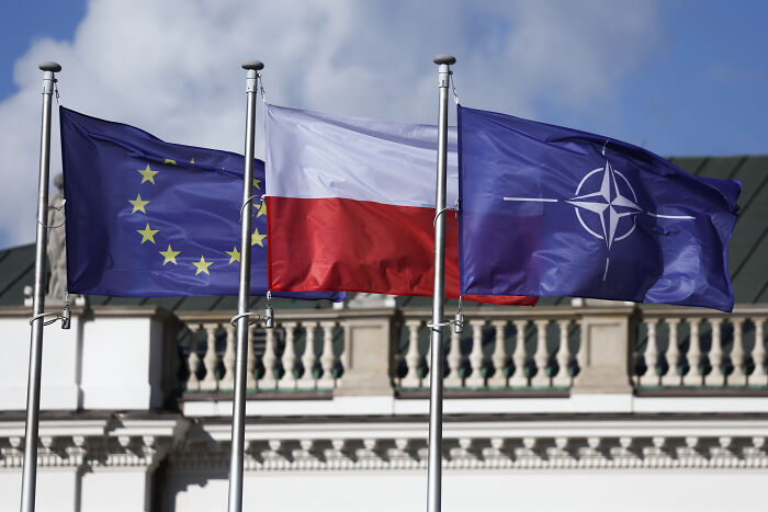 Flags of the European Union, Poland, and NATO flying against a blue sky, symbolizing Poland shooting down Russian drones.