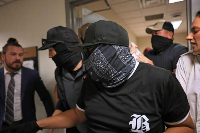 Masked individuals in a secret digital network outing ICE agents, wearing black bandanas and casual clothing indoors.