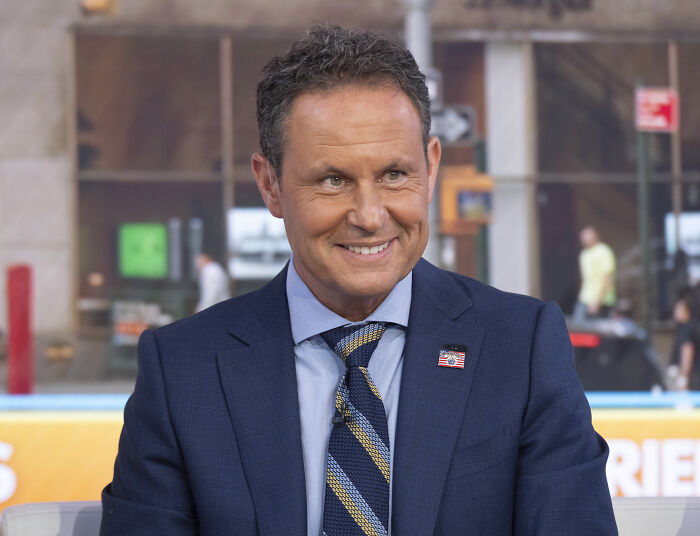 Fox News host in a navy suit and striped tie smiling during an on-air segment, related to controversial comments.