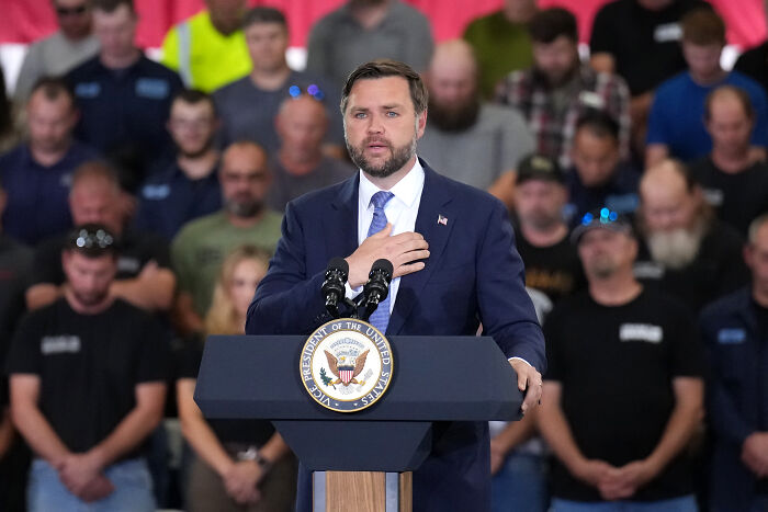 Man in suit speaking at podium with presidential seal, surrounded by audience, illustrating social media impact on Donald Trump.