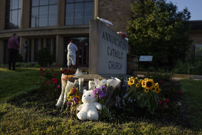Memorial with flowers and teddy bear outside Annunciation Catholic Church related to Minnesota school shooter incident.