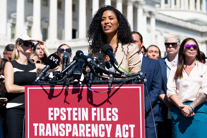 Woman speaking at Epstein victims rally with multiple microphones, highlighting Trump disrupts tearful Epstein victims rally event.