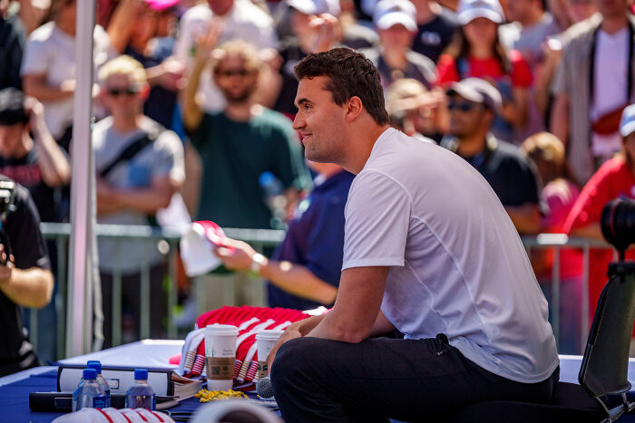 Charlie Kirk speaking at an outdoor event with a crowd, discussing firearm fatalities and related views.