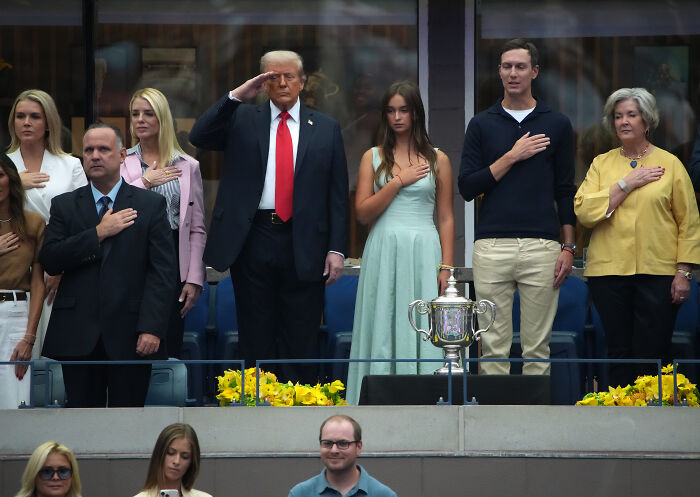 Donald Trump and others standing for the national anthem at the U.S. Open final with a trophy in front.