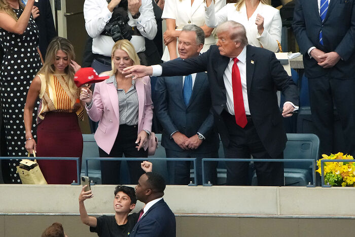 Donald Trump at U.S. Open final, interacting with crowd amid boos and cheers as match start is delayed.