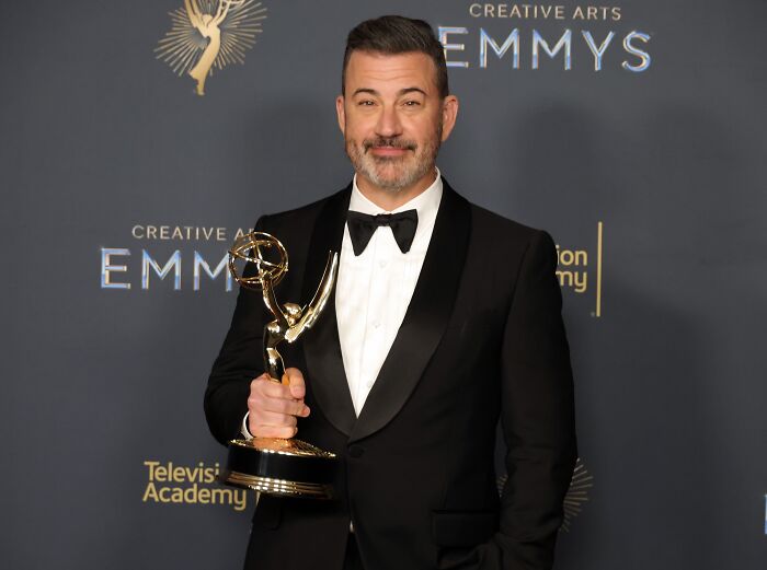 Jimmy Kimmel in a black tuxedo holding an Emmy award, attending a Television Academy Creative Arts event.