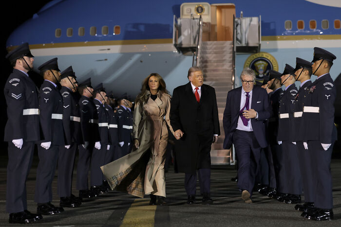 Former President Trump and Melania walking on the tarmac by Air Force One with military personnel standing in formation nearby.