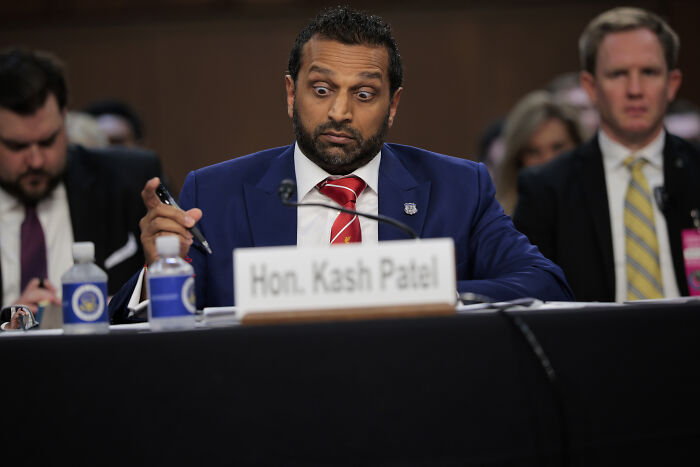Kash Patel in a formal hearing, wearing a blue suit and red tie, reacting dramatically during exchange over Epstein files.