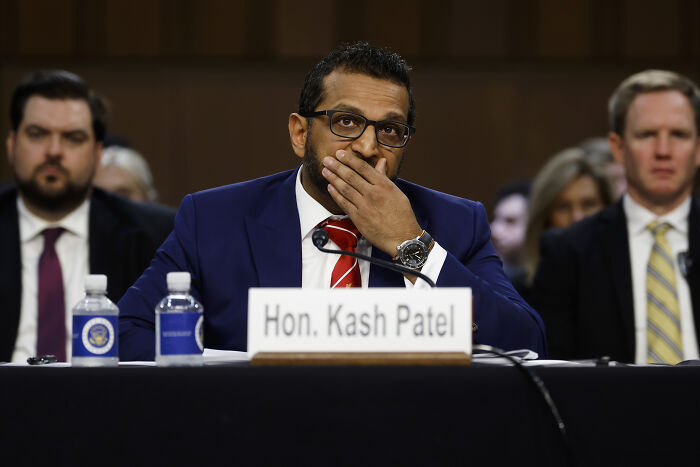 FBI Director Kash Patel at a hearing, wearing glasses and a blue suit, known for handwritten pep talk notes going viral.