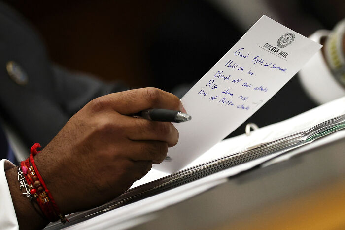Hand holding pen writing handwritten pep talk notes on paper with FBI Director Kash Patel emblem visible.