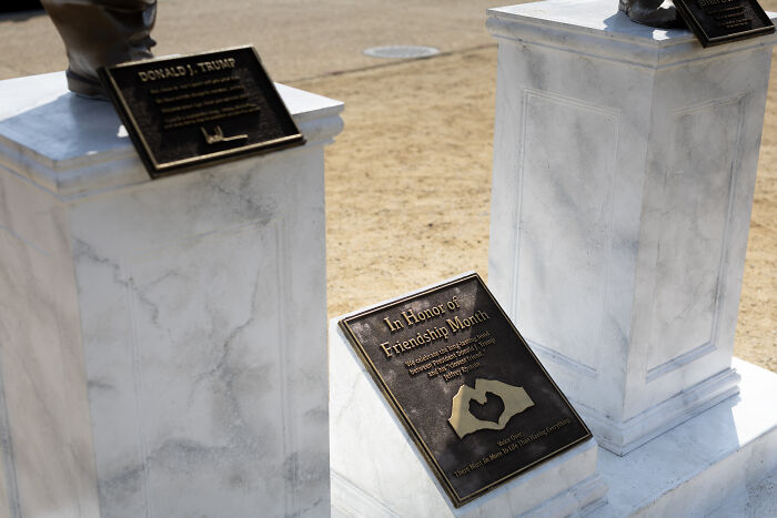 Statues of Trump and Epstein holding hands on white marble pedestals displayed outdoors in D.C.