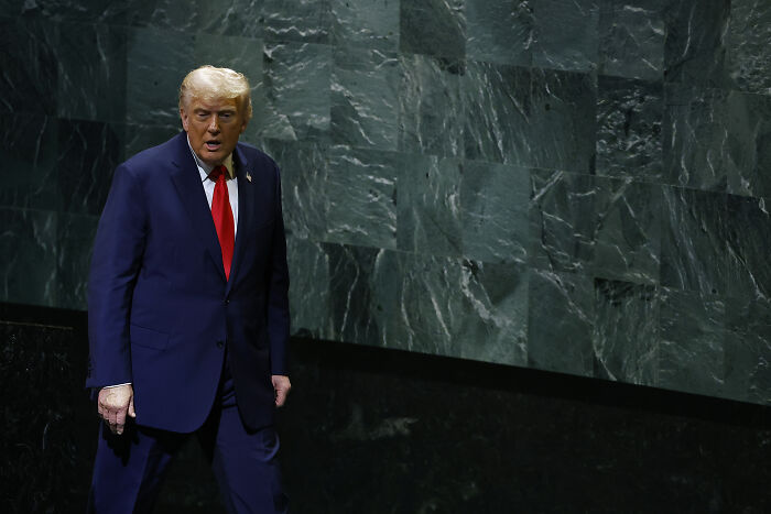Former President Trump in a dark suit and red tie at the UN, after escalator, teleprompter, and speech mic issues.
