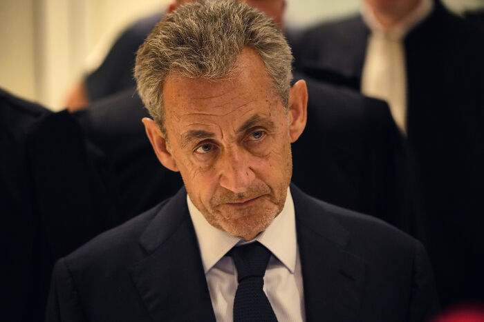 Former French President Nicolas Sarkozy in a dark suit and tie, appearing serious at a public or formal event.