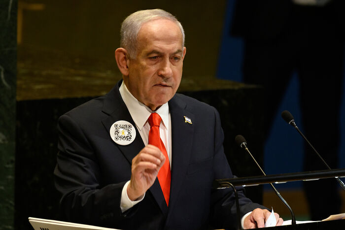 Benjamin Netanyahu speaking at UN General Assembly podium with microphones in a nearly empty auditorium.