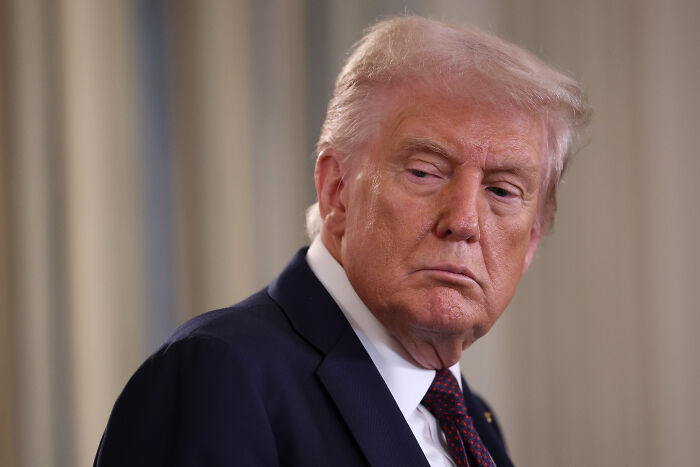 Former President Donald Trump in a suit and tie, looking to the side during an official event addressing Ariana Grande voter post.