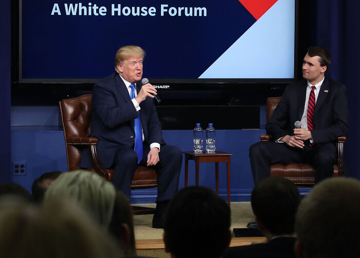 Charlie Kirk speaking at a White House forum, seated and holding a microphone during a discussion on firearm fatalities.
