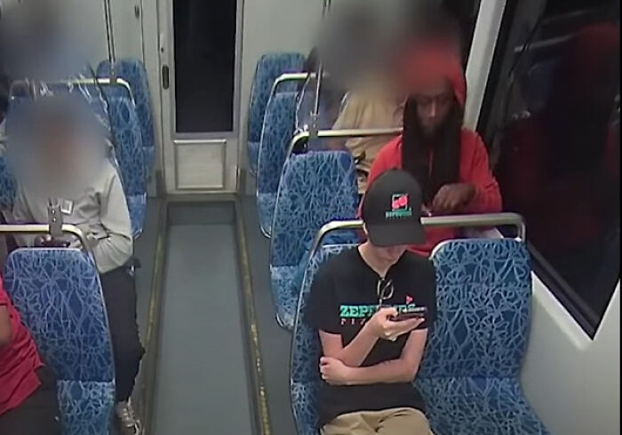 Passengers sitting on a train, with one person wearing a black cap and focused on a phone, related to GoFundMe fundraising pages news.