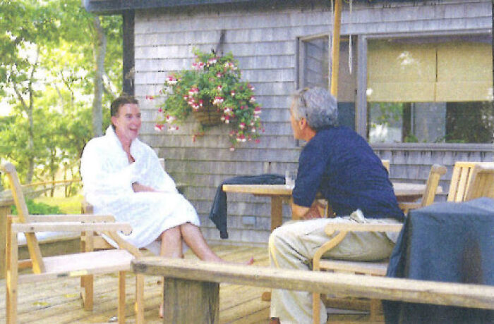 Two men seated outdoors on wooden deck, one wearing white robe, relating to U.S. ambassador fired after Jeffrey Epstein message revealed.