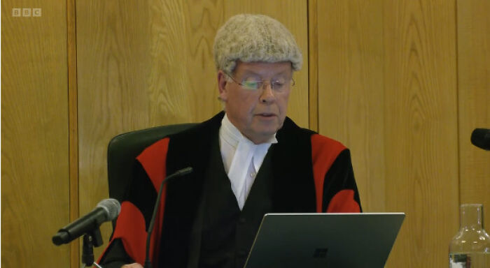 Judge in traditional court attire reading from laptop during trial related to aristocrat Constance Marten case.