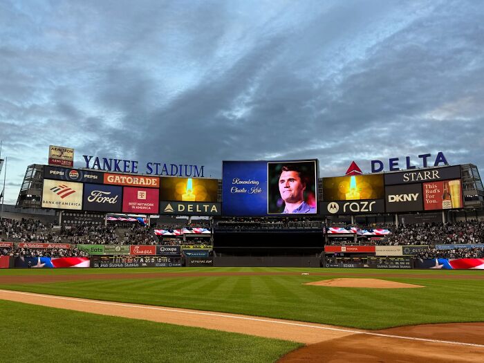 Yankee Stadium scoreboard displaying a tribute image of Charlie Kirk during an evening baseball game.