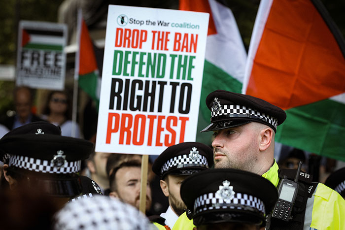 Police officers monitoring a protest with signs defending the right to protest amid debates on free speech social media laws UK.
