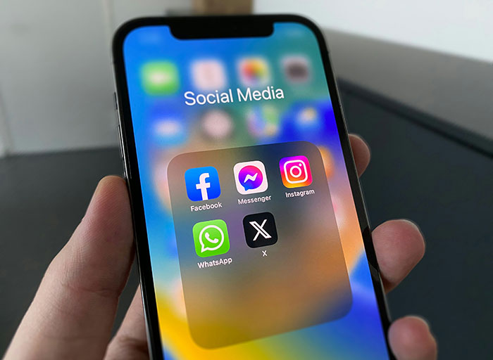 Smartphone screen displaying social media apps including Facebook, Messenger, Instagram, WhatsApp, and X related to free speech social media laws UK.
