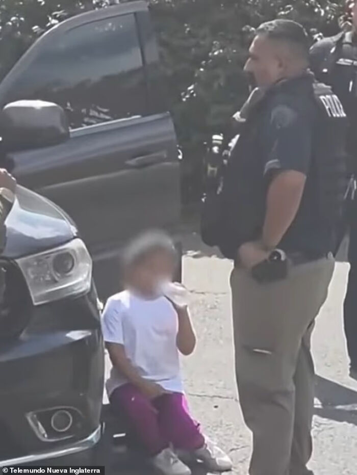 Autistic girl sitting on ground near police officers and vehicles during alleged ICE detention outside a home.