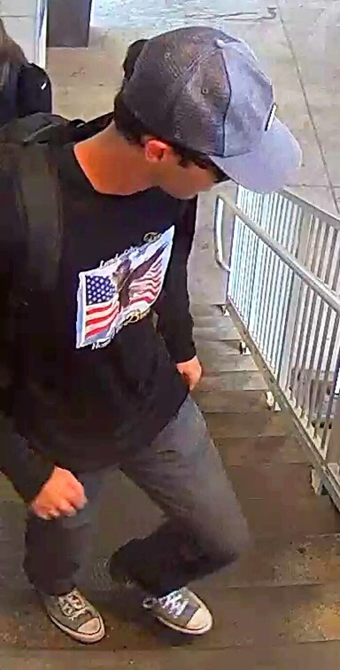 Young man wearing a baseball cap and American flag sweatshirt walking up outdoor stairs in a surveillance-style image related to Charlie Kirk shooting.