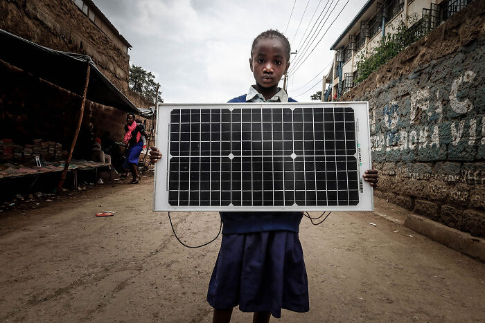 Young girl holding a solar panel on a dusty street, highlighting solar power plant boom in Africa's communities.