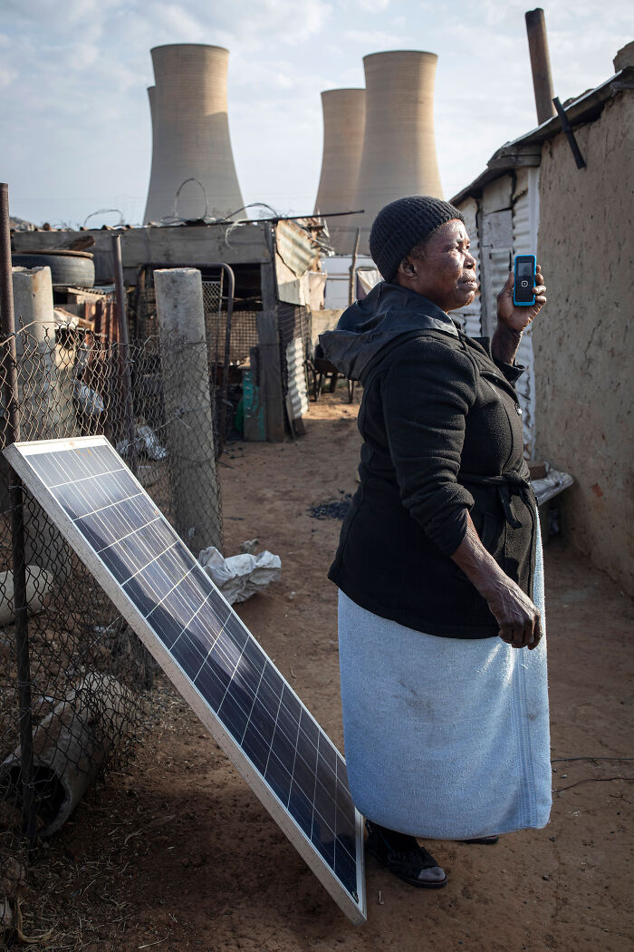 Woman standing next to a solar panel in a rural area with industrial cooling towers in the background supporting solar power plant boom Africa.