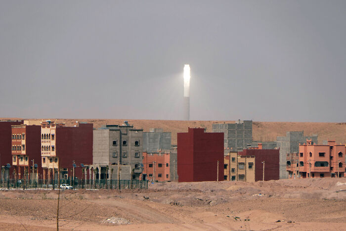 Solar power plant tower reflecting sunlight near a residential area in a dry, desert landscape in Africa.