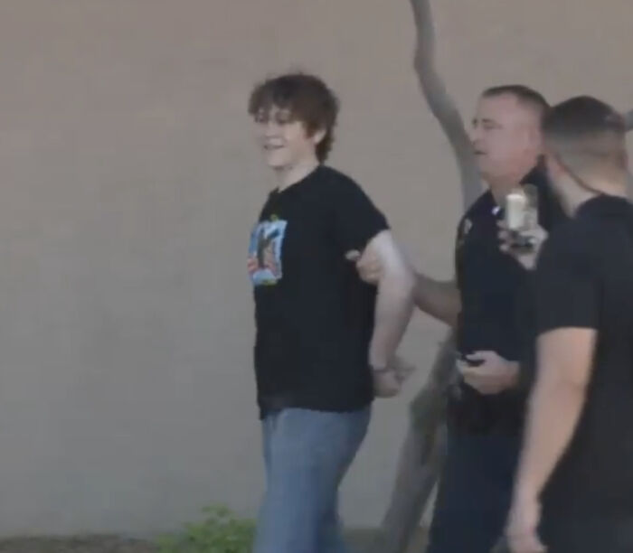 Teen wearing shirt like accused Charlie Kirk shooter, being escorted by police near Turning Point USA event.