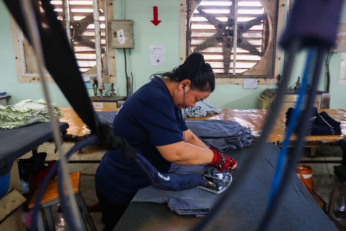 Worker ironing clothes in a factory impacted by Trumps trade war costing billions in lost production and revenue.