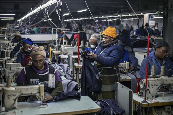 Workers operating sewing machines in a garment factory, illustrating the impact of Trumps trade war costing billions on manufacturing.