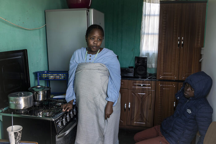 Woman standing by stove in a modest kitchen, illustrating the impact of Trumps trade war costing billions on daily life.