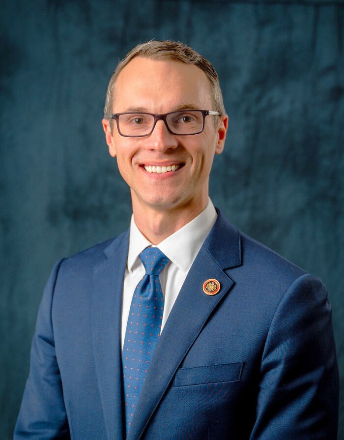 Man in glasses wearing a blue suit and tie, smiling against a dark blue background, representing Democrats narrowing gap in House.