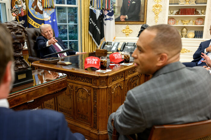 Former President Trump sitting in the Oval Office with Trump 2028 hats on the desk discussing strategy for a third term.