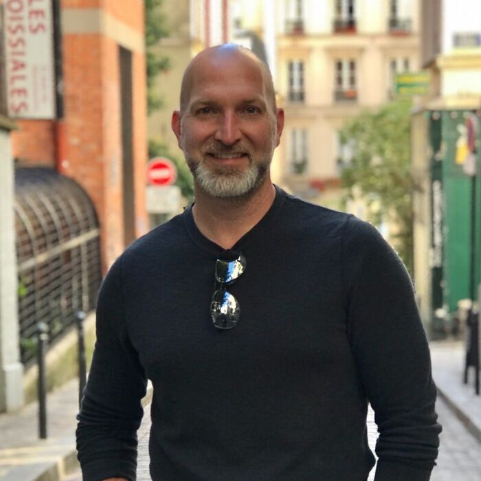 Man with beard and sunglasses hanging on shirt standing on an urban street, related to Halo developers and game-themed ICE recruitment.