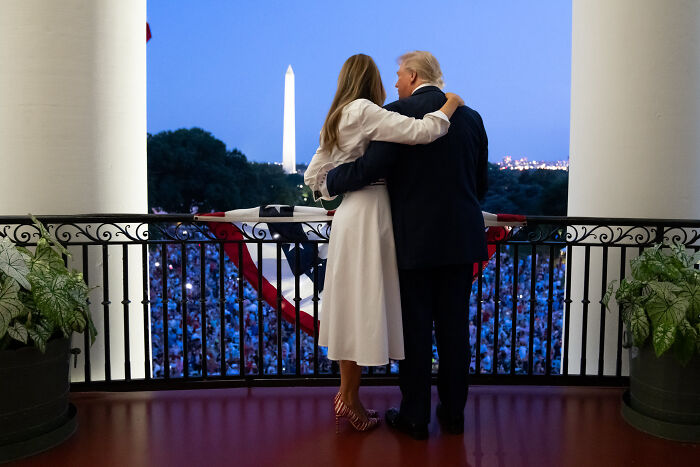 Donald Trump and Melania Trump embracing on balcony with Washington Monument in the background during evening event.